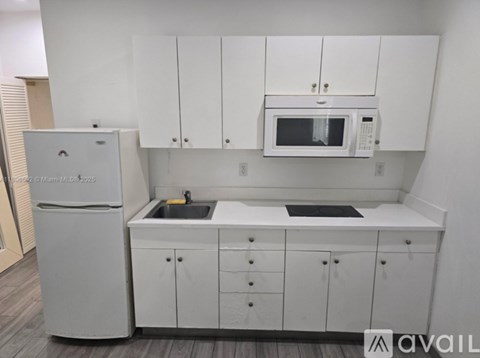 A white kitchen with a fridge, microwave, and sink.