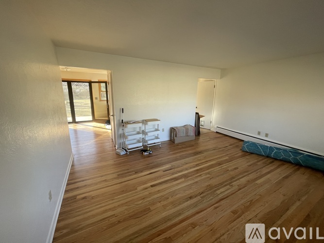 A room with wooden flooring and a white wall with a doorway leading to another room.