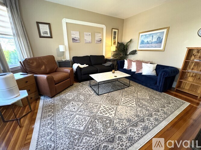A living room with a brown leather chair, a black sofa, a white coffee table, and a rug with a geometric pattern.