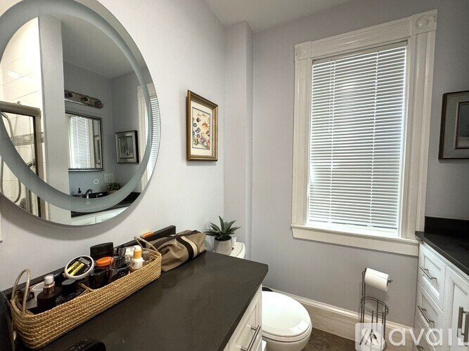 A bathroom with a mirror, a toilet, and a basket of items on the counter.