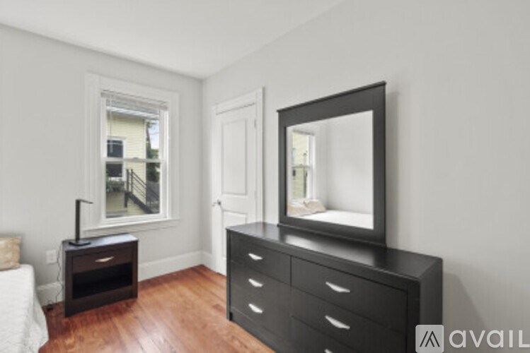 A black dresser with a mirror and a small table with a lamp on it.