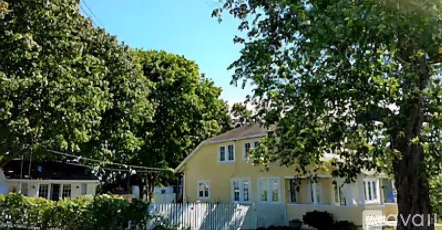 A yellow house with a white fence and trees in the background.