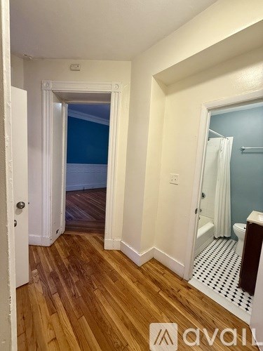 A hallway with wood floors and white walls leading to a bathroom.