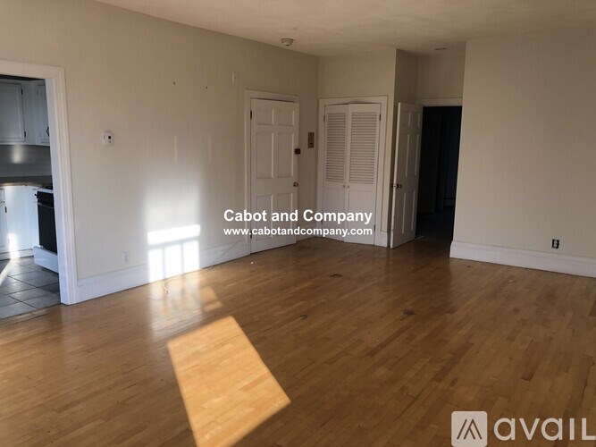 A room with wooden flooring and white walls, with a website address for Cabot and Company displayed on the wall.