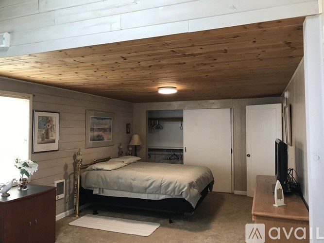 A bedroom with a bed, dresser, and a wooden ceiling.