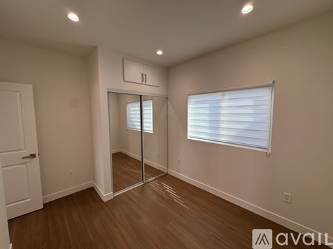 A room with a white door, a window with blinds, and a wooden floor.