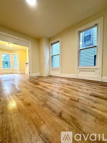 A room with wooden flooring and two windows.