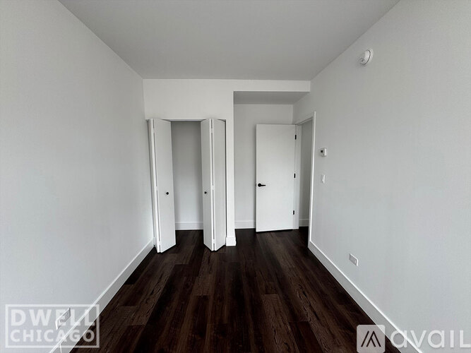 A room with white walls and dark wood flooring, with a door on the right and another door in the middle of the wall.