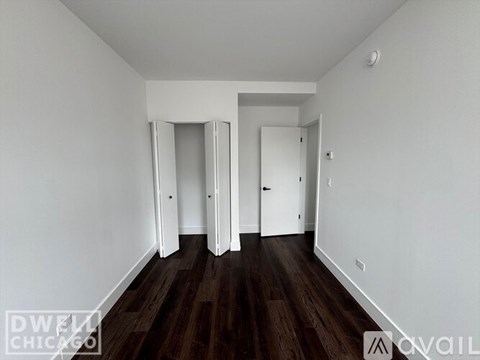 A room with white walls and dark wood flooring, with a door on the right and another door in the middle of the wall.