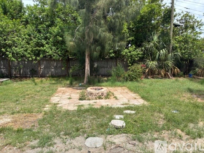 A backyard with a fire pit surrounded by grass and trees.