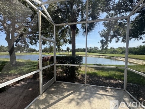 A white metal structure with a glass door is in the foreground of a scenic view with a lake, trees, and a clear sky.