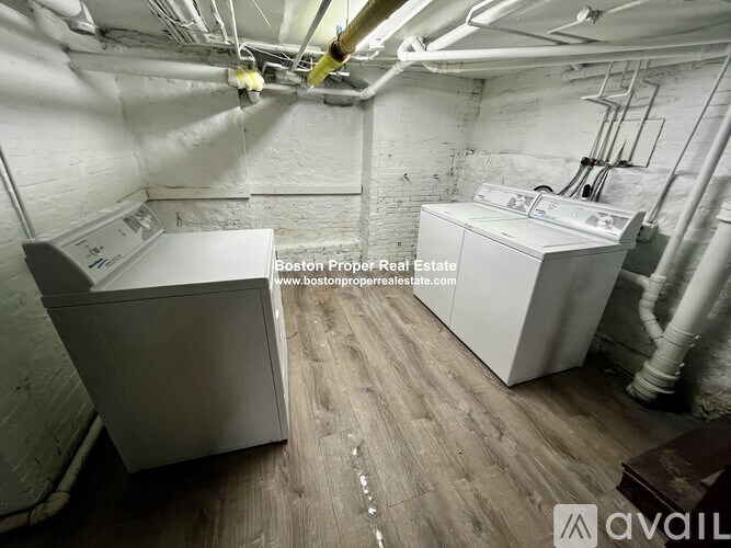 A large industrial-style room with white walls and wooden flooring, containing two large white appliances.