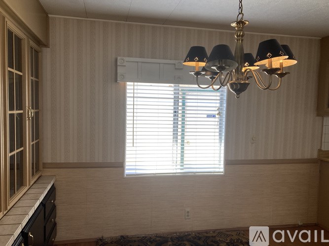 A chandelier hangs in a room with a window covered in blinds.