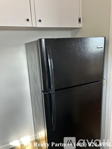 A black fridge in a kitchen with white cabinets.