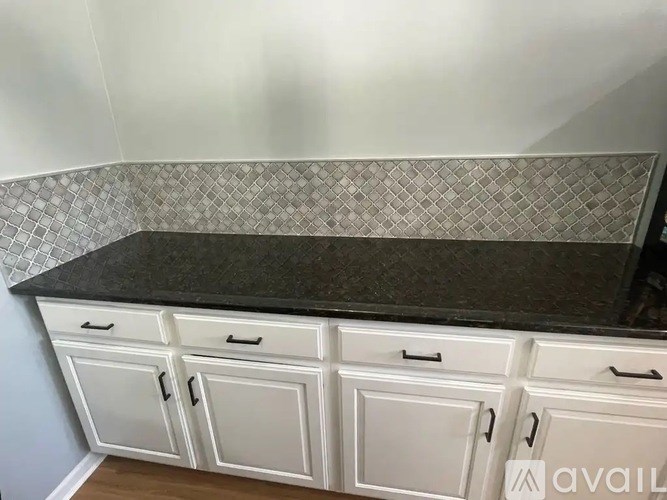 A kitchen counter with white cabinets and a black countertop.