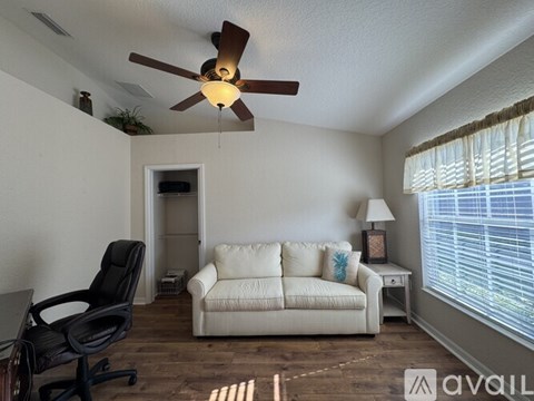 A living room with a white couch, a black chair, and a ceiling fan.