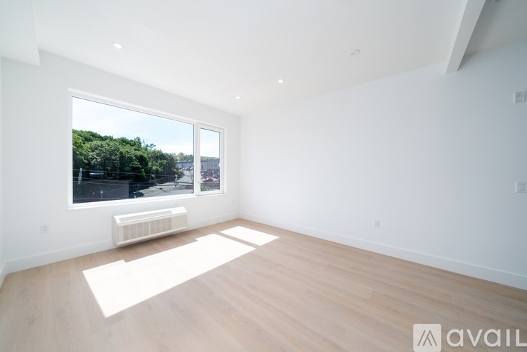 A spacious room with wooden flooring and a large window overlooking a green landscape.