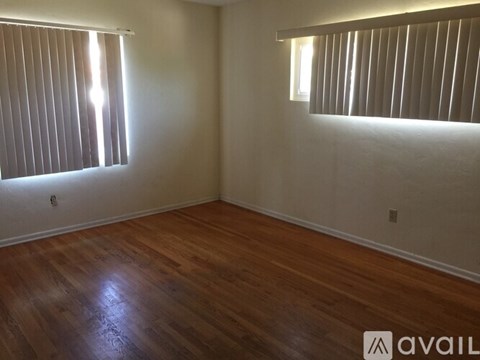A room with wooden floors and two windows with blinds.