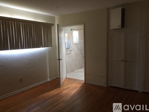 A room with wooden floors and white walls, with a door open to another room.