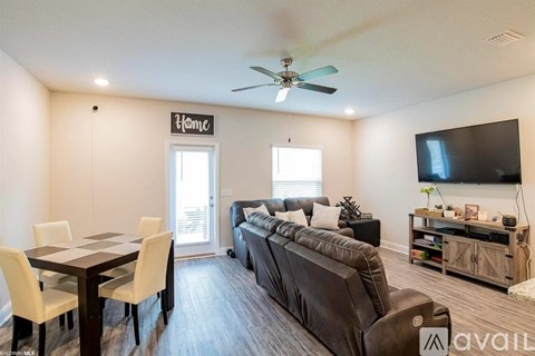 A living room with a brown couch, a dining table with chairs, and a flat-screen TV mounted on the wall.