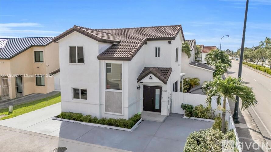 A white house with a brown roof is surrounded by other houses.