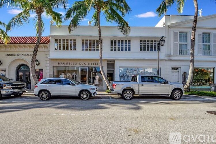 Two silver cars are parked in front of a white building with a red roof.