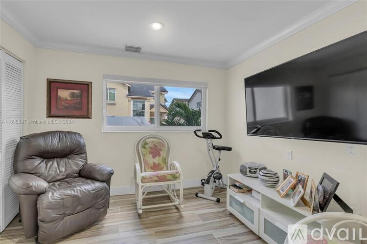 A living room with a grey leather chair, a white chair with a floral pattern, a television, and a window with a view of a building and trees.