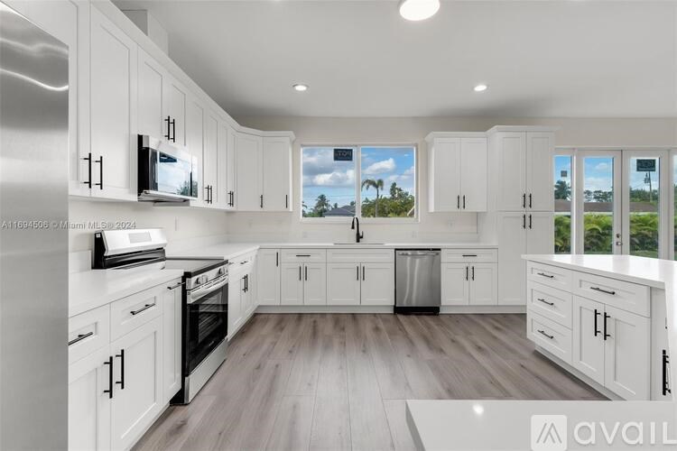 A modern kitchen with white cabinets and a wooden floor.