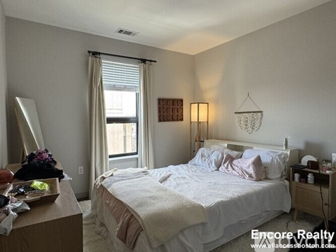 A bedroom with a bed, nightstand, and window with curtains.