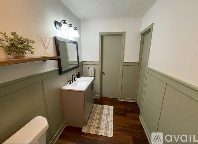 A bathroom with a toilet, sink, mirror, and a shelf with a plant.