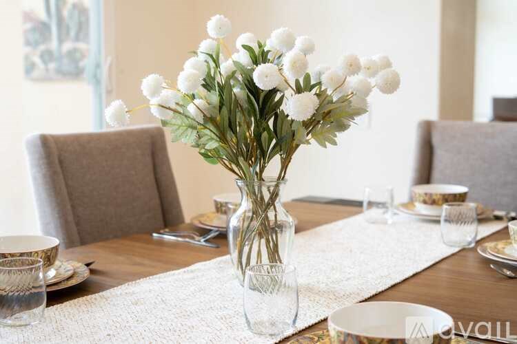 A dining table set with a vase of white flowers in the center.
