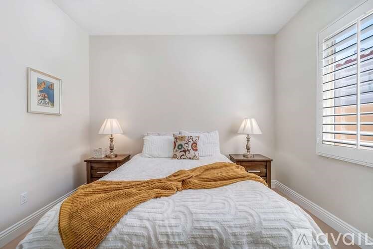 A bedroom with a bed, two lamps, and a picture on the wall.