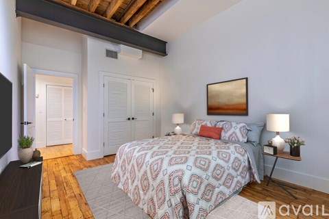 A bedroom with a patterned bedspread and a painting on the wall.