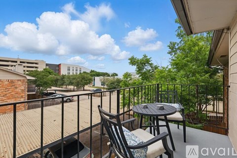 A balcony with a table and chairs overlooks a parking lot and buildings.