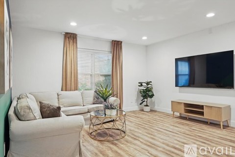 A living room with a white sofa, a TV, and a plant.