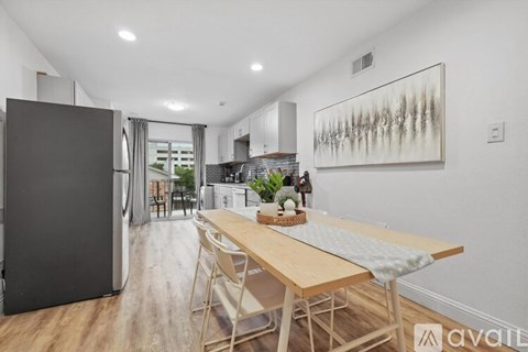 A kitchen with a wooden table and chairs, a refrigerator, and a painting on the wall.