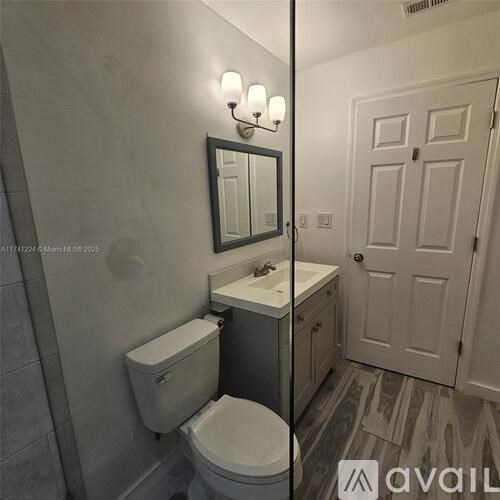 A bathroom with a toilet, sink, mirror, and a door.