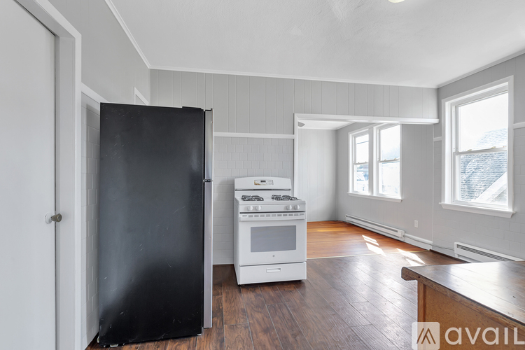 A kitchen with a black refrigerator, white stove, and wooden floors.