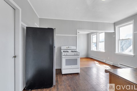 A kitchen with a black refrigerator, white stove, and wooden floors.