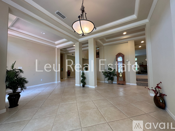 A spacious hallway with a chandelier and a plant on the left side.