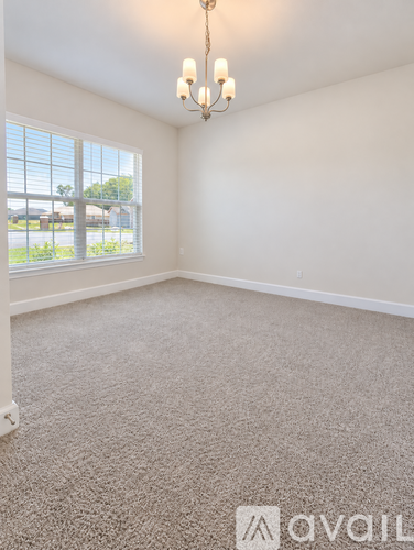 A room with a carpeted floor, a chandelier, and a large window.