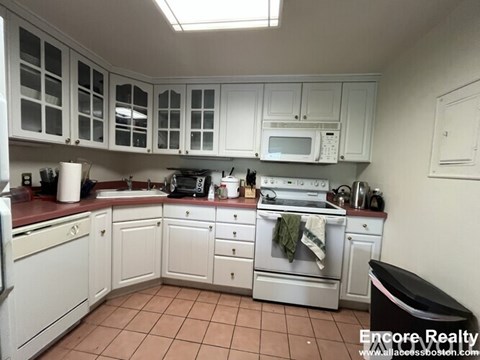 A kitchen with white cabinets and a black trash can.
