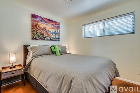 A bedroom with a bed, a nightstand with a lamp, and a painting on the wall.