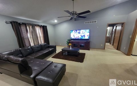 A living room with a black leather sofa and a television on the wall.