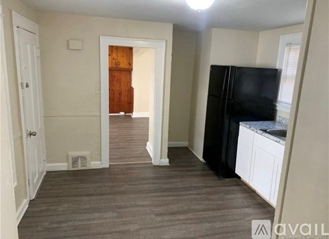 A kitchen area with a black fridge, white cabinets, and a wooden door in the background.