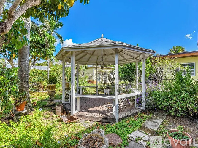 A gazebo is surrounded by green plants and trees.