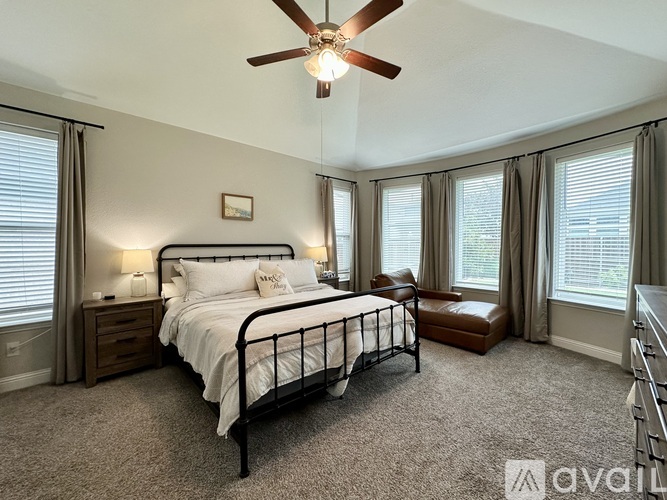 A bedroom with a large bed, a ceiling fan, and a window with curtains.
