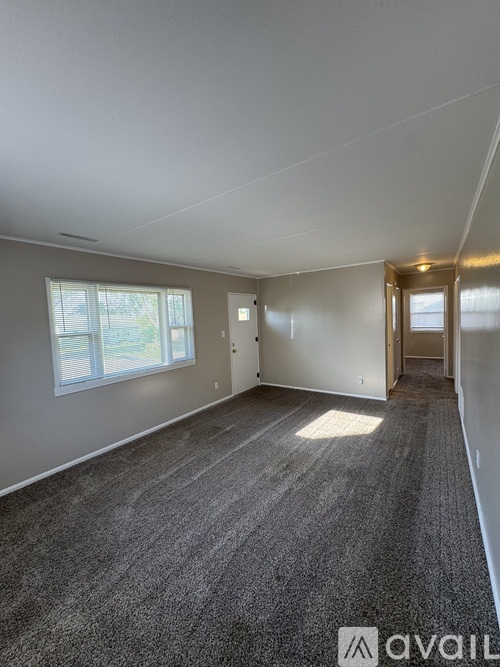 A spacious room with grey carpeting and a window with blinds.