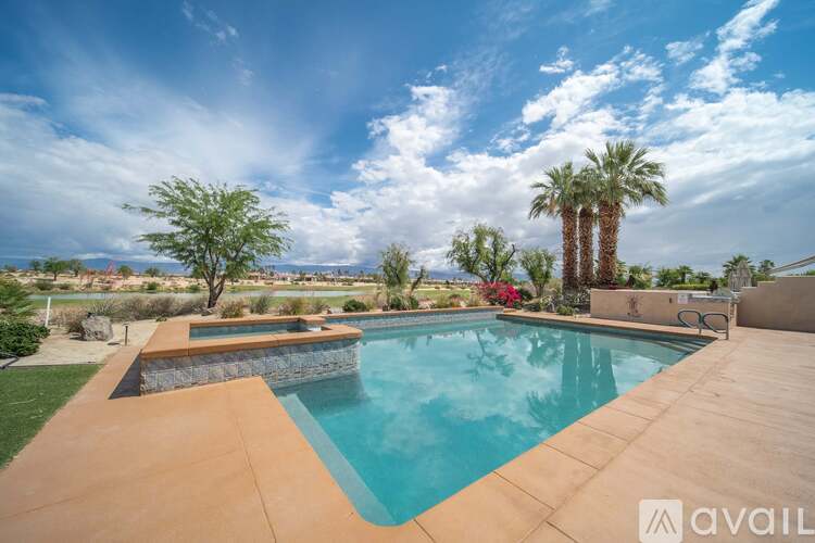 A pool surrounded by a concrete patio and a stone wall.