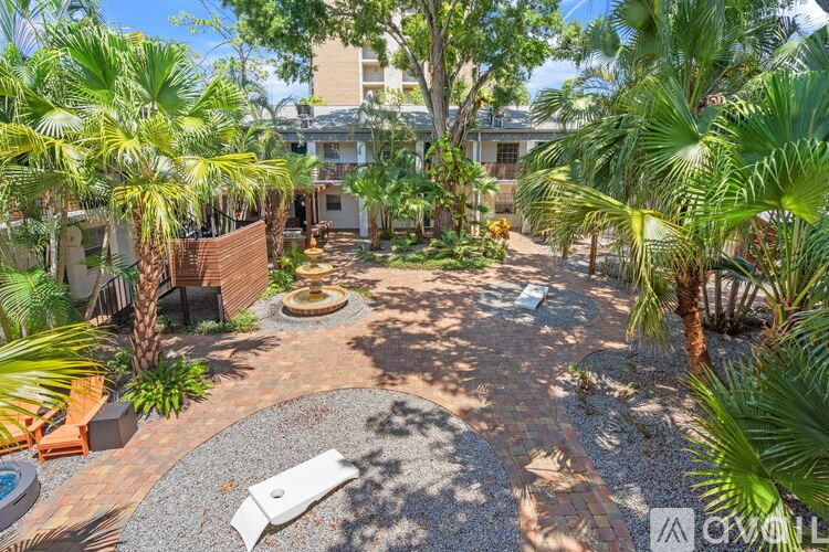 A backyard with a circular patio and a fire pit surrounded by palm trees.